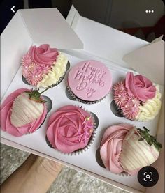 four cupcakes with pink frosting and white icing are in a box