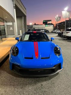 a blue sports car parked in front of a parking lot at night with lights on