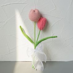 two crocheted flowers in a vase with white ribbon tied around the stems, against a white painted wall