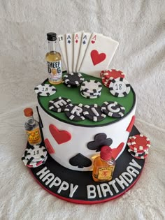 a birthday cake decorated with playing cards, chips and liquor on a white tablecloth