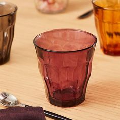 three different colored glasses sitting on top of a wooden table next to spoons and utensils