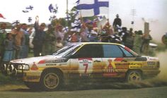 a car driving down a dirt road with flags flying in the air and people watching