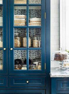 a blue china cabinet with glass doors and baskets on the top, in a kitchen