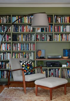 a chair and ottoman in front of a book shelf with books on the wall behind it