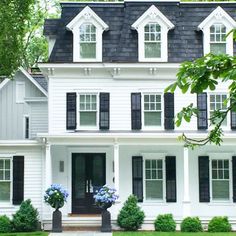 a white two story house with black shutters and flowers on the front lawn in front of it