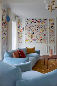 a living room filled with blue couches and colorful paintings