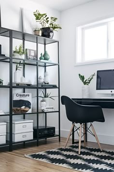 a desk with a computer on top of it next to a book shelf filled with plants