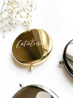 a compact mirror with the word catalina written on it sitting next to a small flower