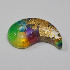 a gold dragon brooch sitting on top of a white table next to a rainbow colored object