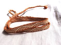 an orange and white braided bracelet on top of a white cloth covered tablecloth