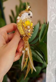 a hand holding a gold colored bird ornament with pearls on it's tail