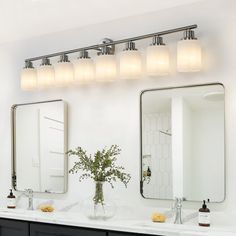 a bathroom with two sinks, mirrors and lights on the wall above them are flowers in a vase