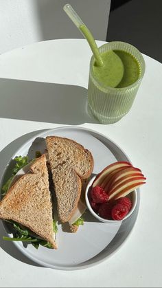 a white plate topped with a cut in half sandwich next to a bowl of fruit