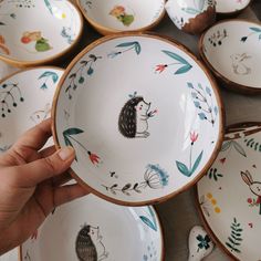 a hand holding a hedgehog bowl in front of many other plates on the table