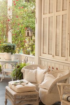 a porch with wicker furniture and potted plants on the back deck, surrounded by white shutters