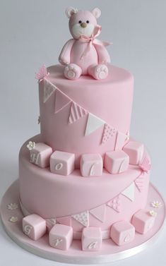 a pink cake with a teddy bear on top and other decorations around the edges,