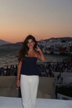 a woman standing on top of a roof next to the ocean at sunset with people in the background