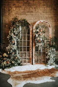 two arched windows decorated with flowers and greenery in front of a brick wall, surrounded by snow