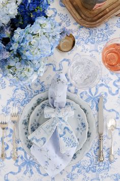 a blue and white table setting with napkins, silverware and flowers on it