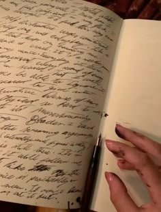 a hand holding a pen over an open book with writing on the pages in cursive ink