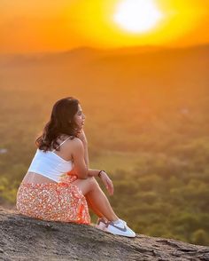 a woman sitting on top of a rock next to a forest under a yellow sky