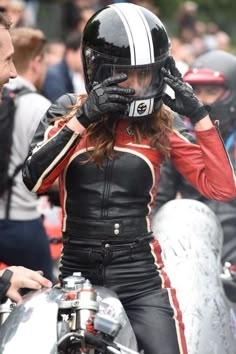 a woman in black and red leather outfit sitting on a motorcycle with her hands to her face