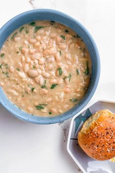 a bowl of soup next to a roll on a white table with a blue rim