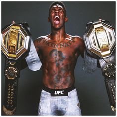 a man holding two gold and black wrestling belts with his mouth wide open while standing in front of a gray background