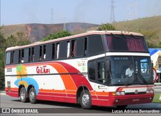 a red, white and orange bus driving down a street with mountains in the background