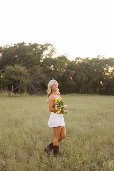 a woman in a white dress is standing in tall grass with flowers on her bouquet