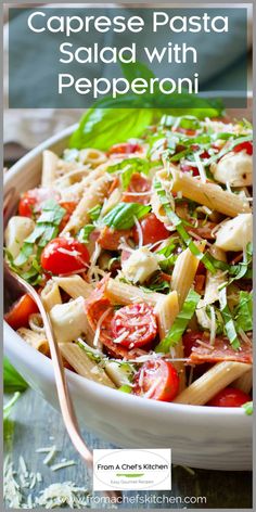 a pasta salad with tomatoes, cheese and spinach in a white bowl on top of a wooden table