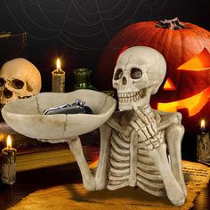 a skeleton holding a bowl in front of two pumpkins and candles on a table