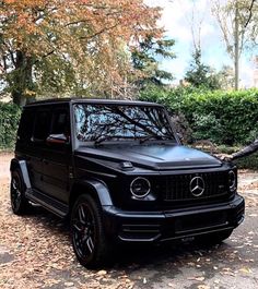 a man standing next to a black mercedes g - class parked in front of trees