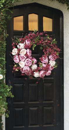 a black front door with pink and white flowers on the wreath hanging from it's side