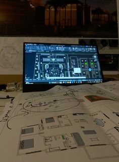 a laptop computer sitting on top of a table covered in blueprints and drawings