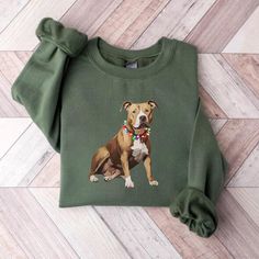 a green sweatshirt with a brown and white dog on it's chest sitting on a wooden floor