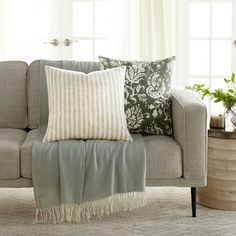 a living room with a gray couch and pillows on top of the couch, along with potted plants