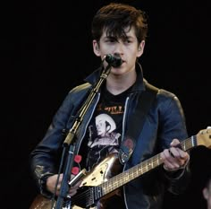 a young man holding a guitar and singing into a microphone