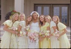 a group of women standing next to each other in front of a building holding bouquets