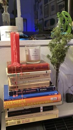 a stack of books sitting on top of a table next to a vase and candle