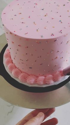 a pink cake with sprinkles on it being held by a person's hand