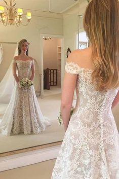 a woman in a wedding dress looking at herself in the mirror with her hair back to the camera