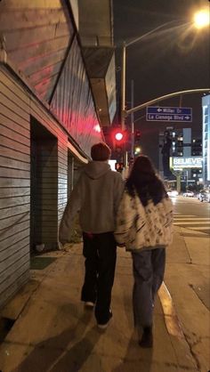 two people are walking down the sidewalk at night, one is holding his arm around the other's back