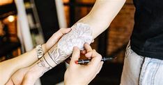 two people with tattoos on their arms holding onto one another's arm and writing something on the other hand