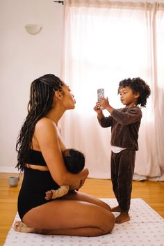 a woman holding a baby and taking a photo with her cell phone while sitting on the floor