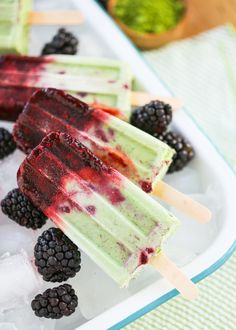 three popsicles with blackberries and raspberry toppings on top of ice