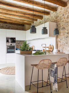 a kitchen with two bar stools next to an island and potted plants on the counter