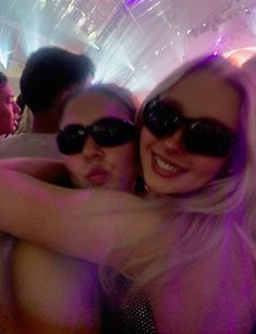 two women hugging each other in front of a crowd at a party with lights on the ceiling