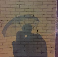 the shadow of a person holding an umbrella is projected on a brick wall behind them