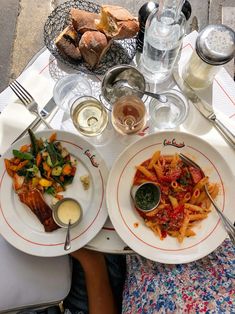 two plates of food on a table with utensils and wine glasses next to them